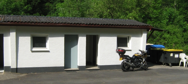 a white small toilet and shower block with my bike in front of it at the campsite in cocham